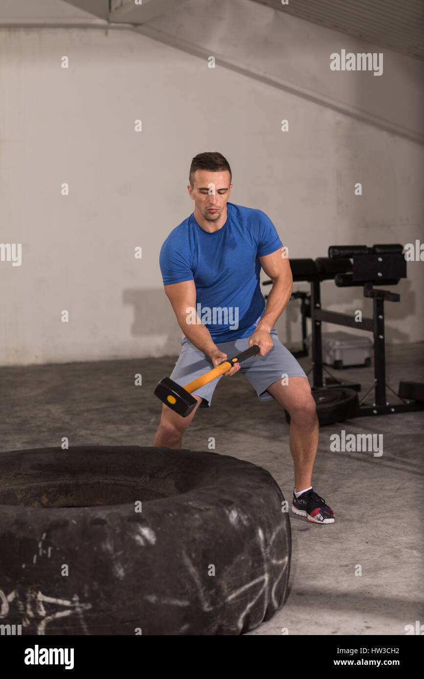 Sledgehammer Tire Hits young muscular man workout at gym with hammer