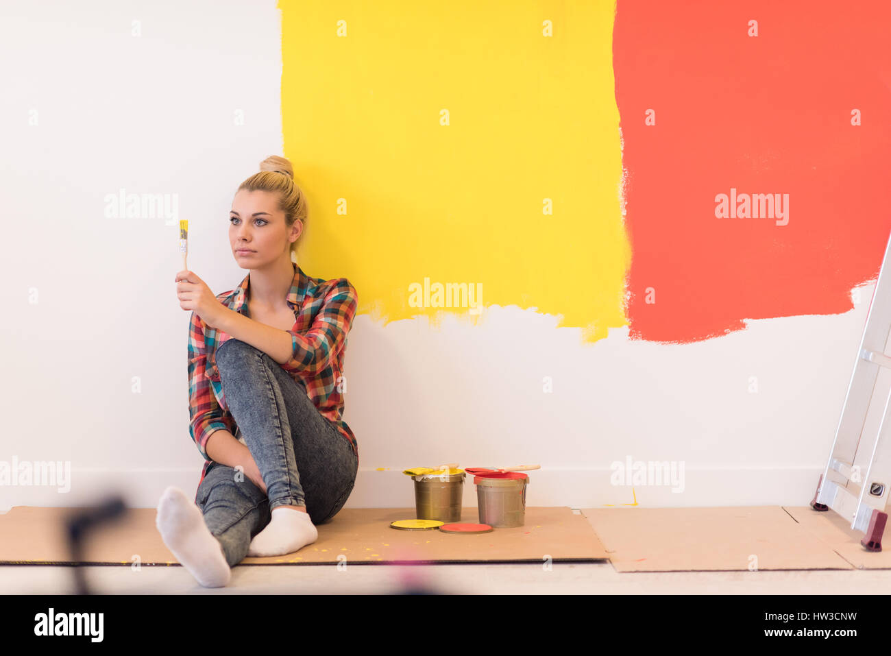 Portrait of a beautiful young female painter sitting on floor near wall ...