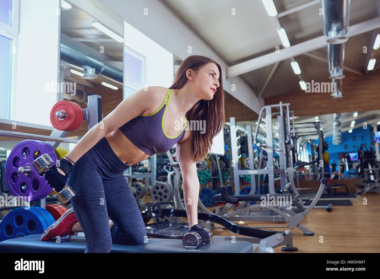 Young sporty girl with dumbbells in hands doing exercises in spo Stock Photo