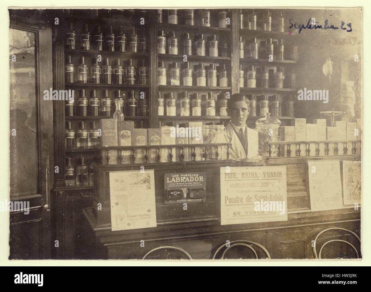 Antique photograph of interior of pharmacy shop displaying jars of drugs and medicines, man - owner, staff or assistant, dispensing, in France dated September 1929 Stock Photo