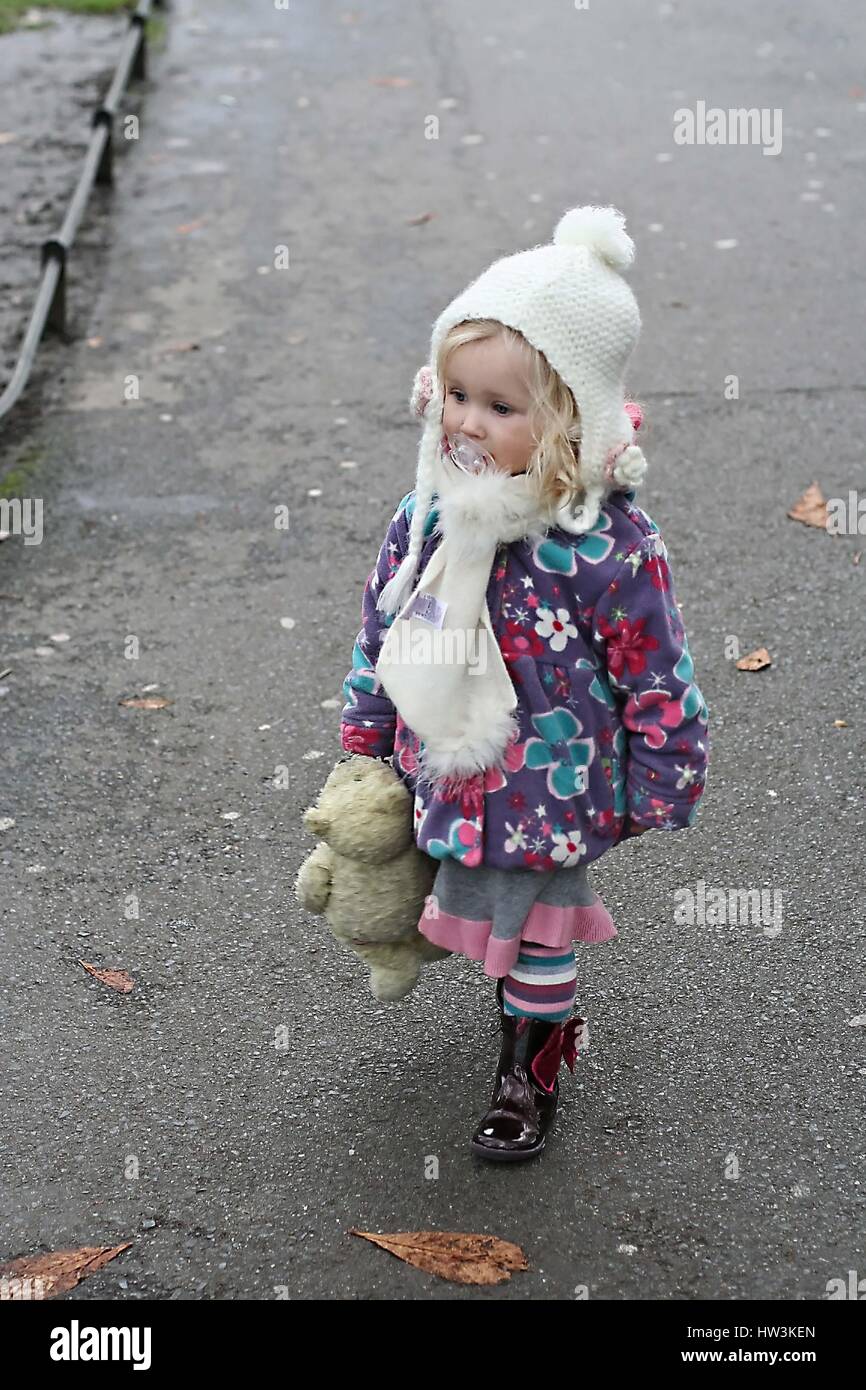 Little girl holding her teddy bear running park St. Stephen's Green Dublin Ireland toddler exploring, teddy dodie, hat scarf, cold day concept winter Stock Photo