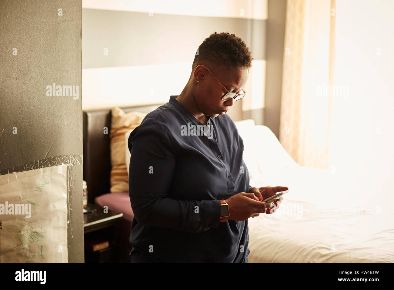 Black woman standing in bedroom texting on cell phone Stock Photo