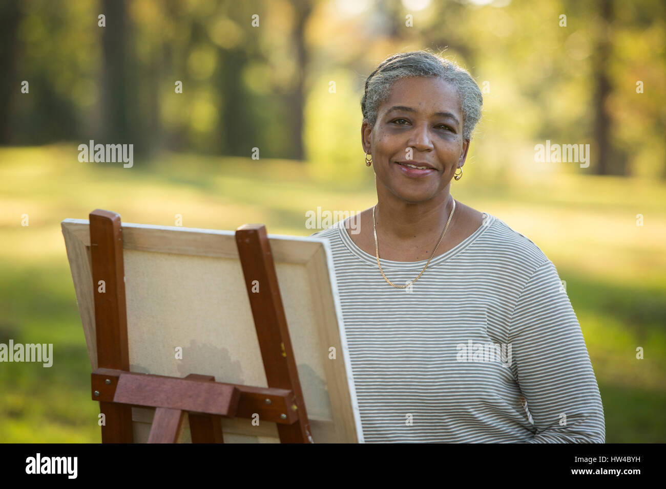 Portrait of Black woman painting on canvas in park Stock Photo