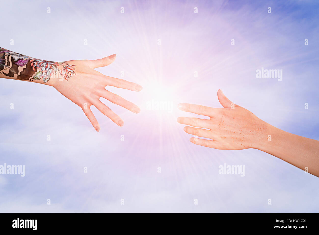 Hands with tattoos and freckles reaching in sky Stock Photo