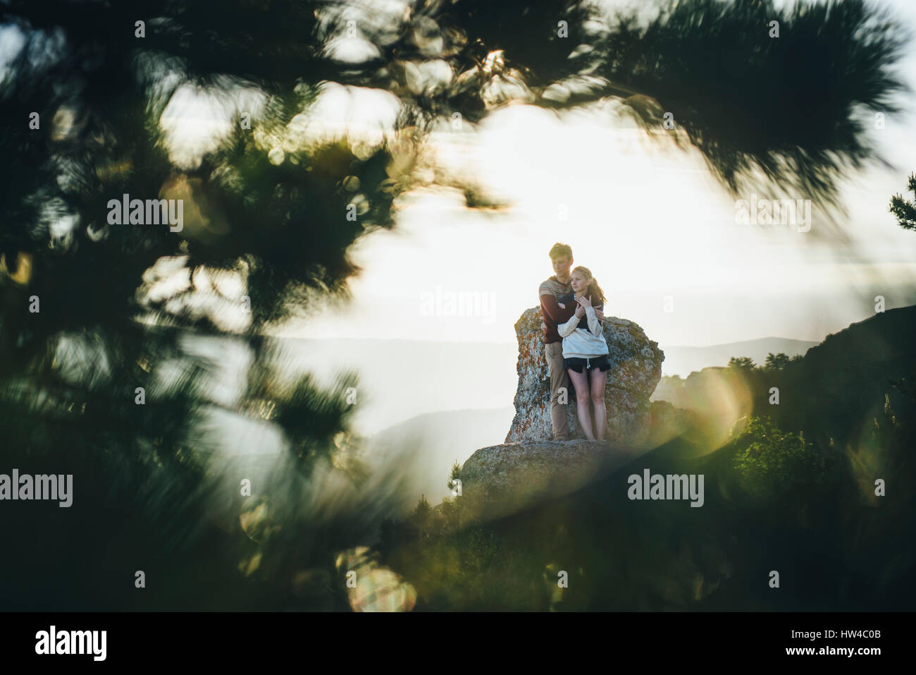 Tree branches framing Caucasian couple hugging at rock Stock Photo