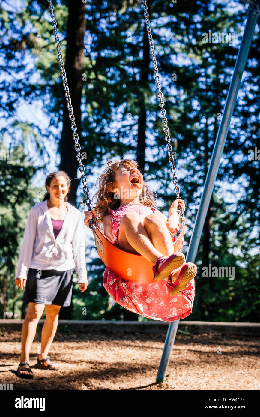 Caucasian mother pushing daughter on playground swing Stock Photo