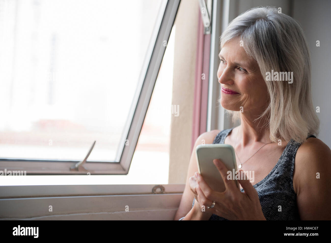 Smiling Caucasian woman texting on cell phone near window Stock Photo