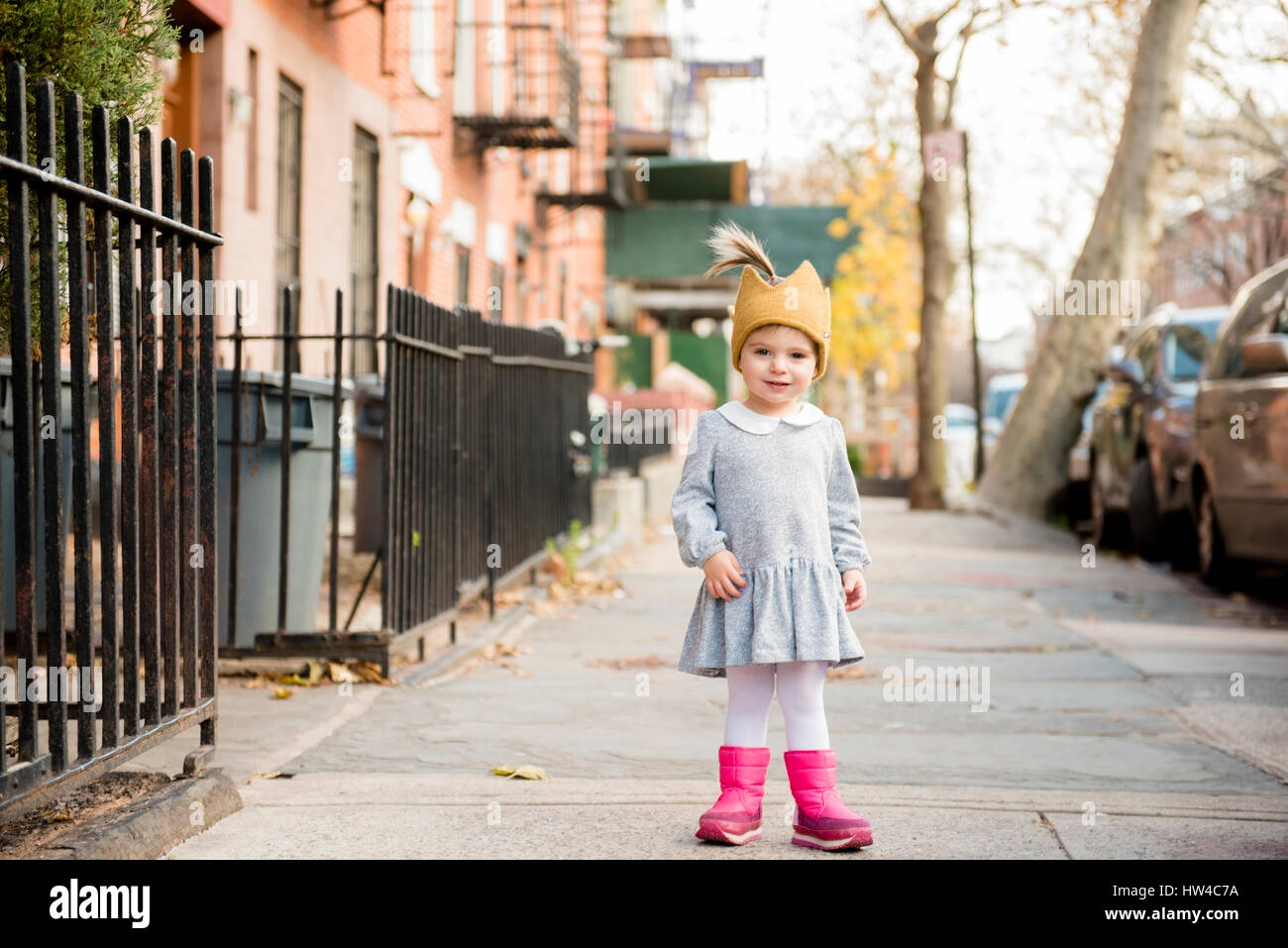 Smiling Caucasian baby girl wearing crown hat on city sidewalk Stock Photo