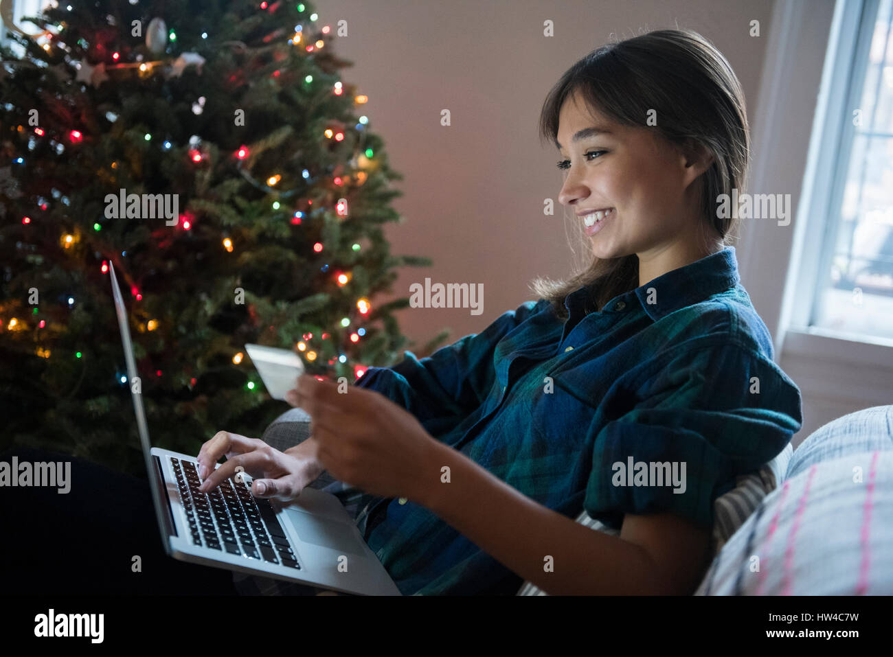 Mixed Race woman online shopping with laptop near Christmas tree Stock Photo