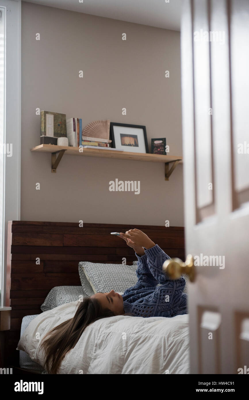 Mixed Race woman laying on bed texting on cell phone Stock Photo