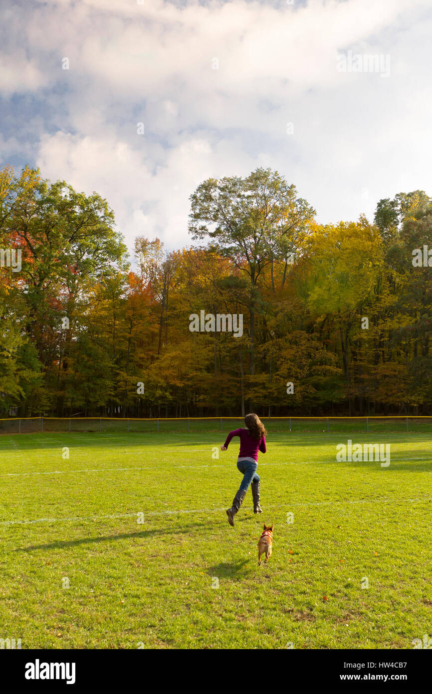 Caucasian woman running with dog in field Stock Photo