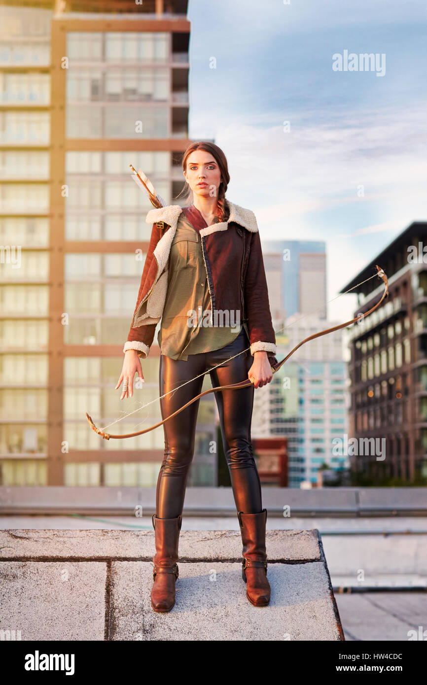 Mixed race woman with bow and arrow on urban rooftop Stock Photo