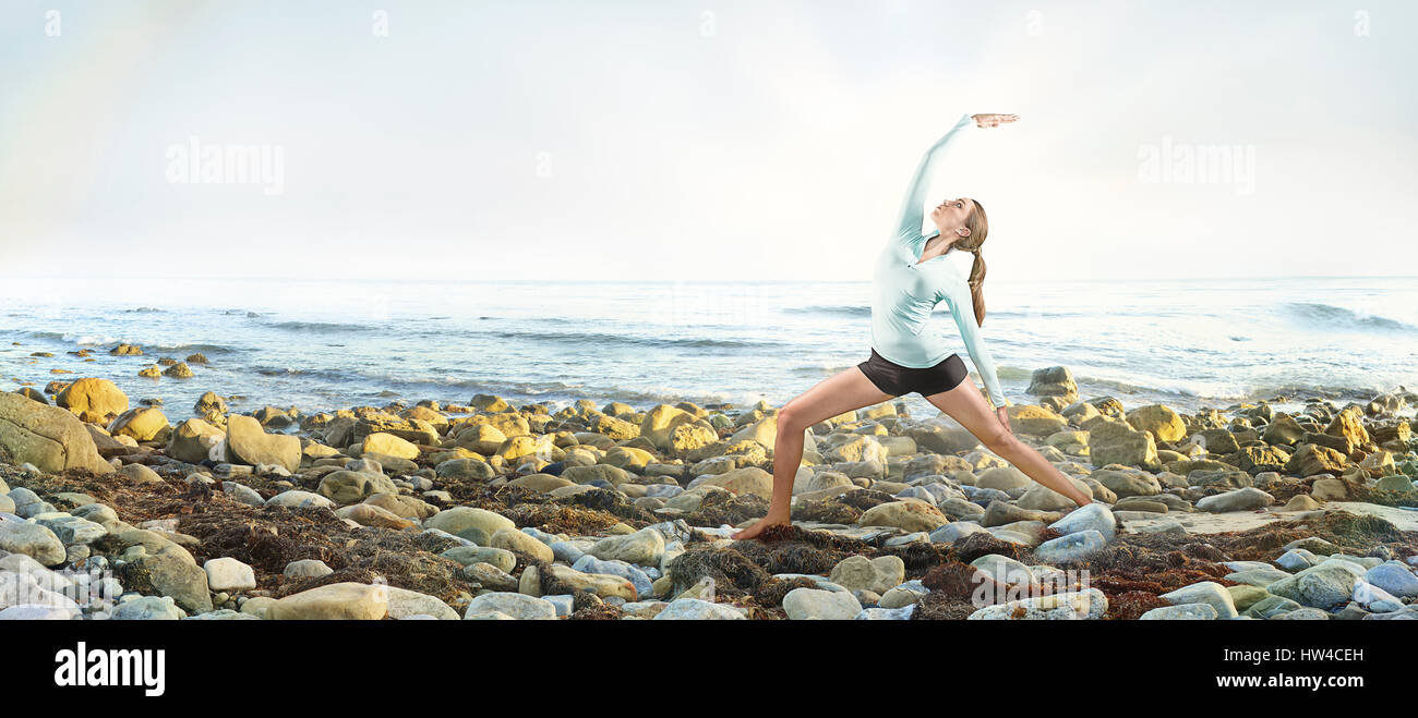 Mixed race woman practicing yoga on rocky beach Stock Photo