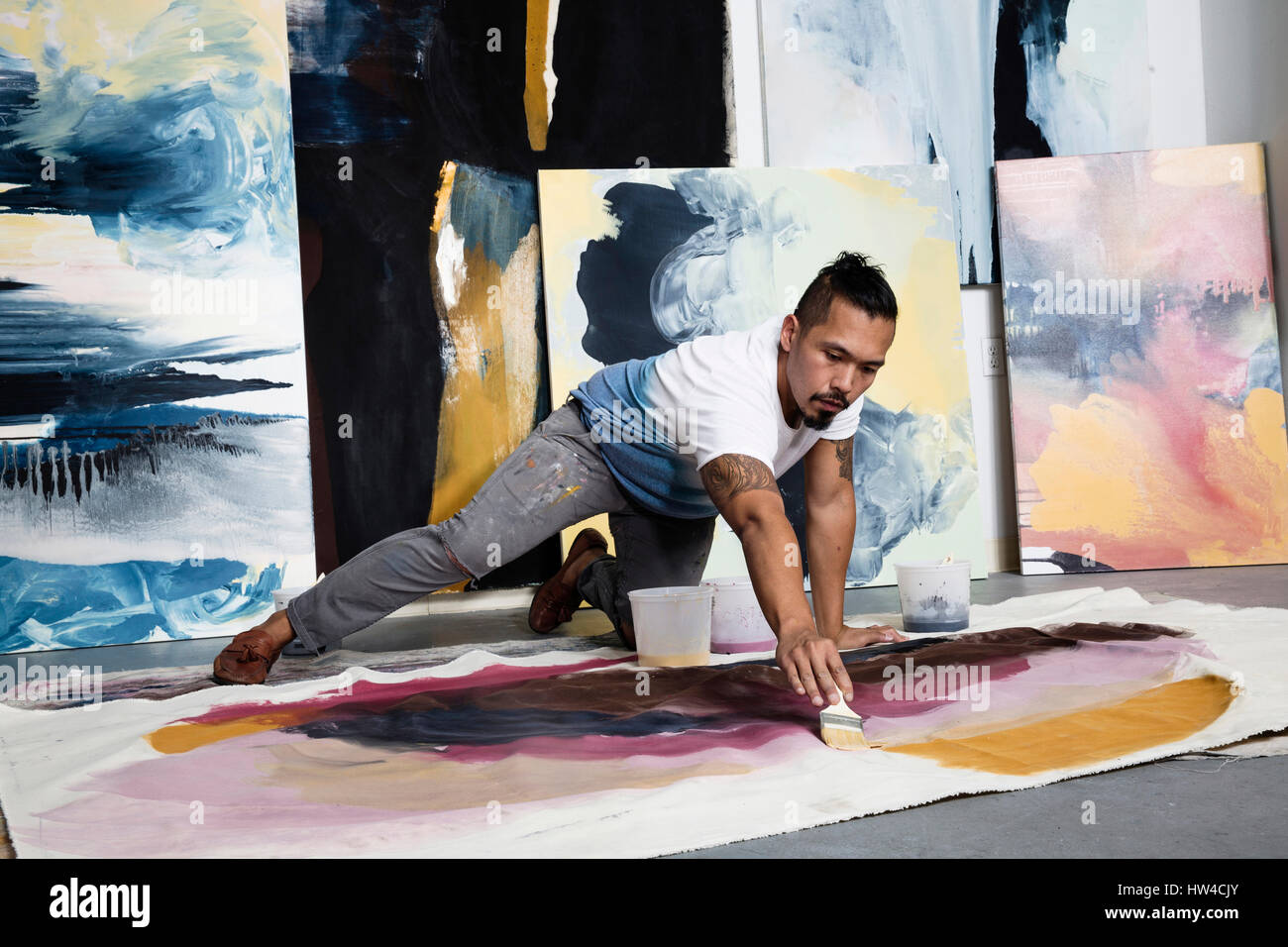 Pacific Islander artist kneeling on floor painting on canvas Stock Photo