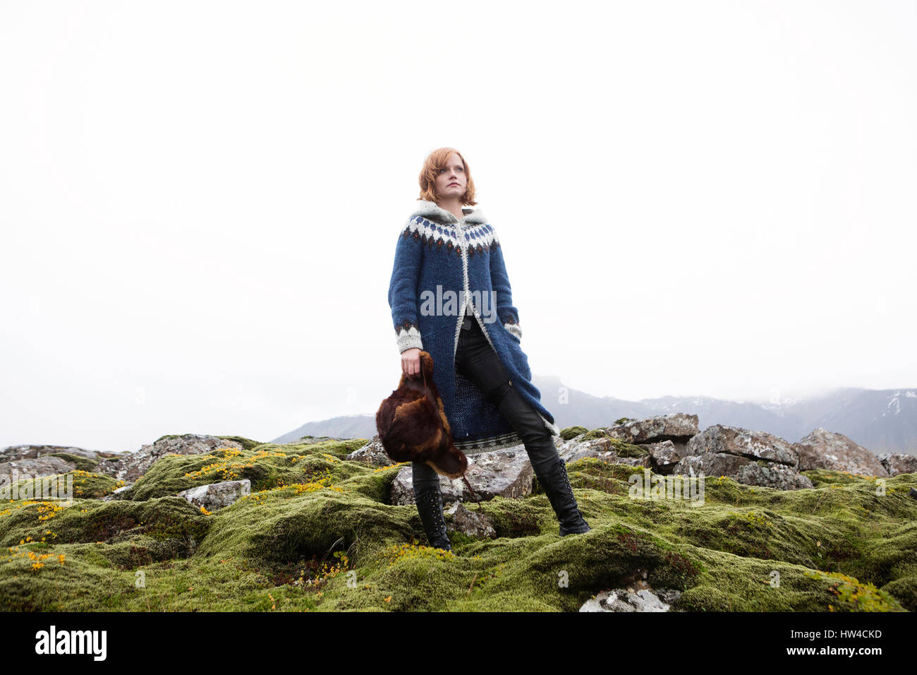 Caucasian woman standing on mossy rocks holding fur hat Stock Photo