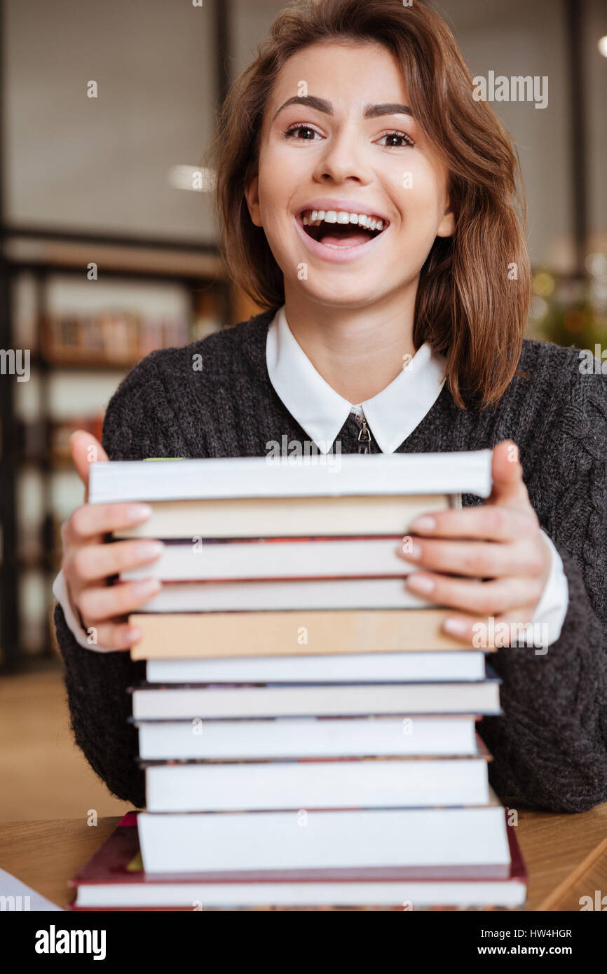 Smiling young female student with stack of books in library Stock Photo ...