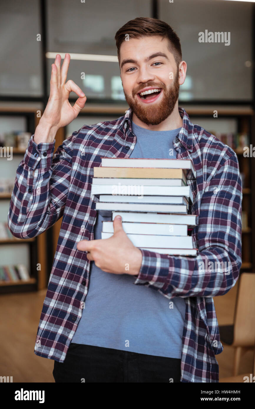 Portrait of a happy attractive man student holding books in library and ...