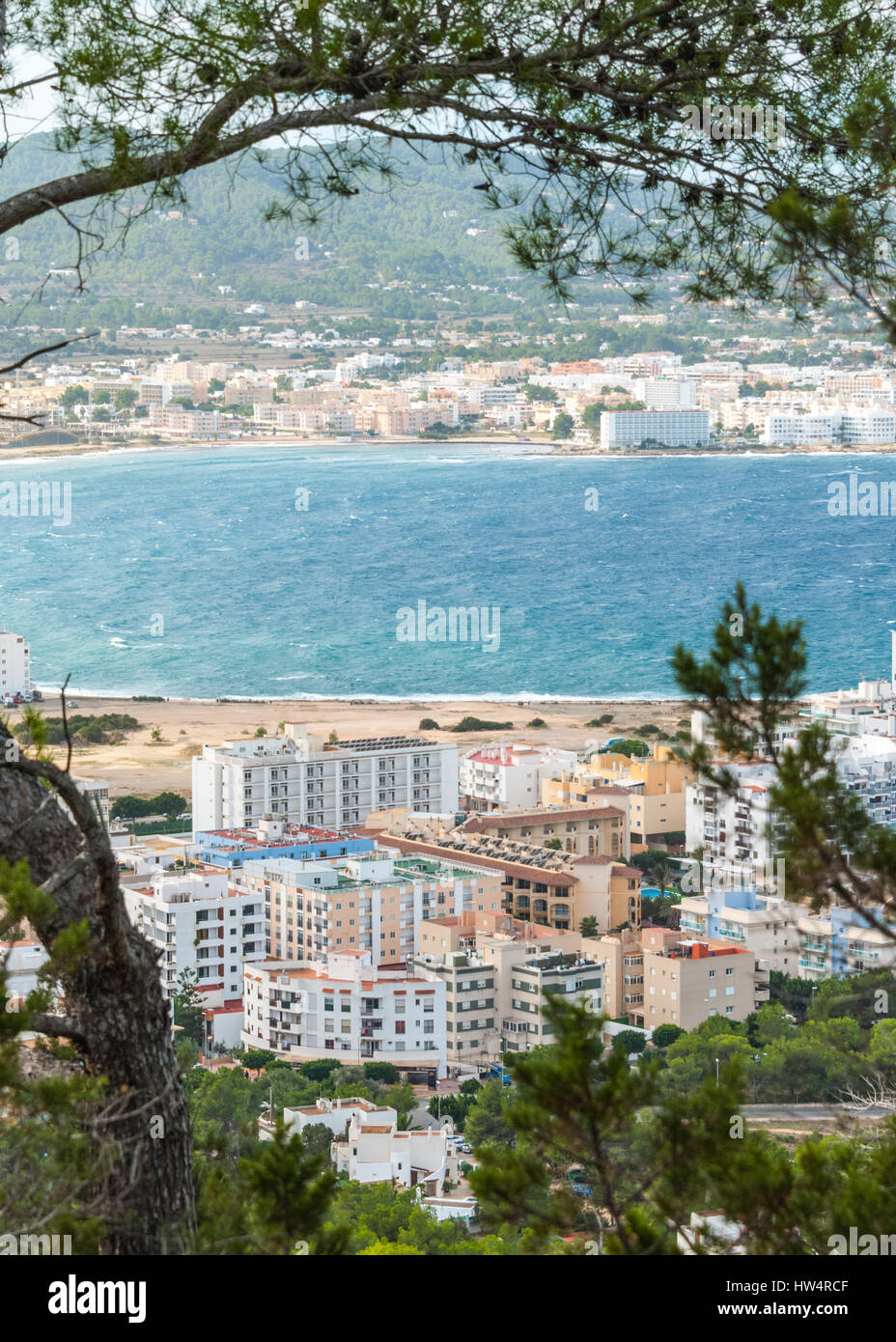 View through naturally framing trees, from hillside of nearby town: San Antonio Sant Antoni de Portmany in the Balearic Islands, Ibiza, Spain. Stock Photo