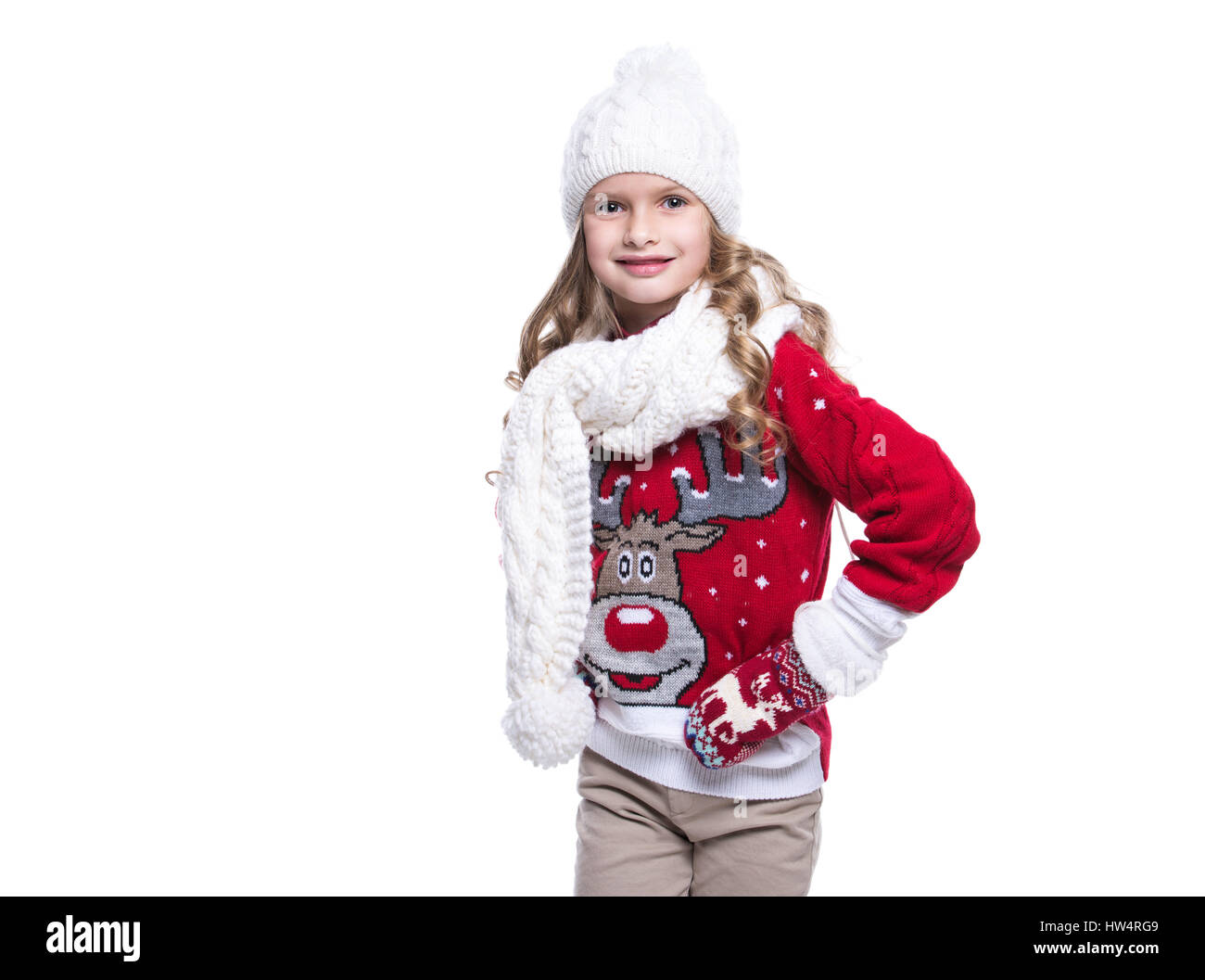 Cute smiling little girl with curly hairstyle wearing knitted sweater, scarf, hat and gloves isolated on white background. Winter clothes Stock Photo