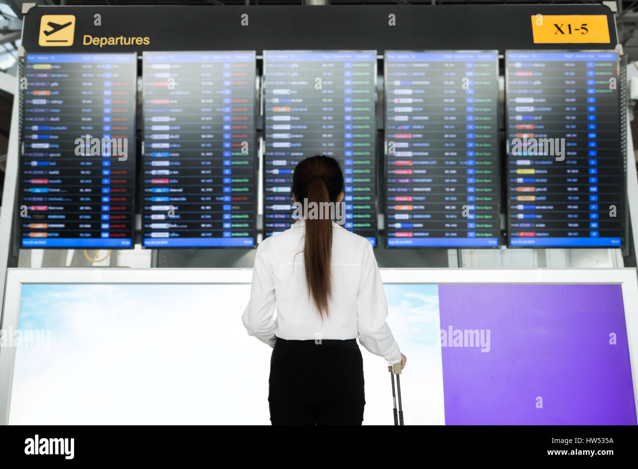 Asian young businesswoman in international airport looking at the flight information board, checking her flight. Stock Photo