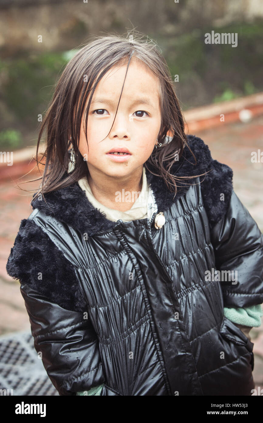 Sapa, Vietnam - May 6, 2014: Portrait of little vietnamese girl in the rainy weather on the street of Sapa village, Northern Vietnam on May 06, 2014. Stock Photo