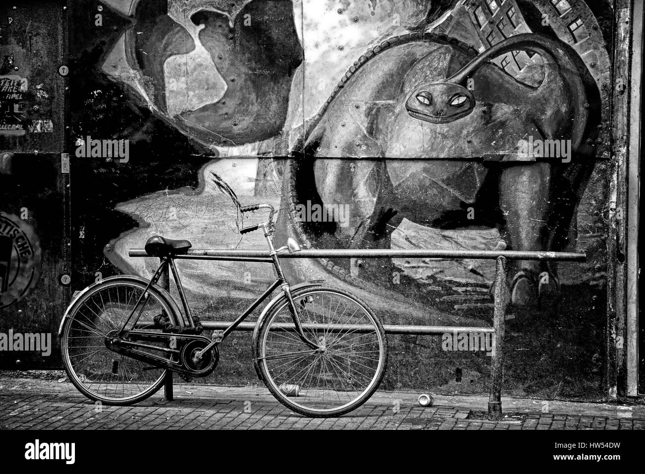 Graffiti artwork of a prehistoric animal appearing to be viewing a bicycle parked in the street. Amsterdam, Netherlands. Stock Photo
