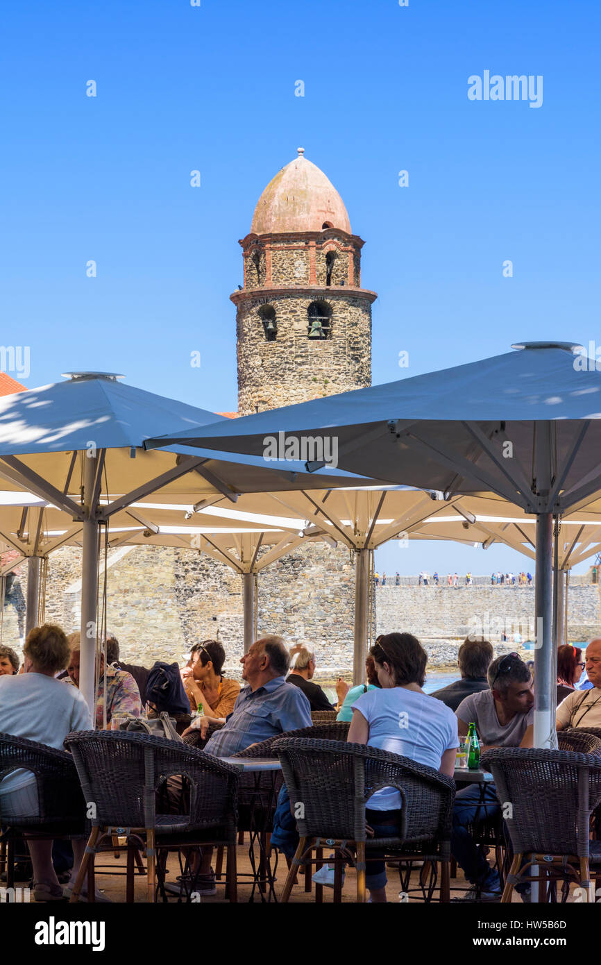Busy beachside cafe overlooked by the bell tower of the Church of Notre Dame des Anges, Collioure, Côte Vermeille, France Stock Photo