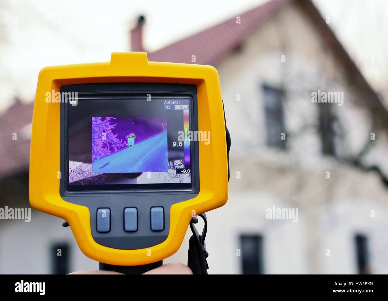 Recording Heat Loss of the Roof on the House with Infrared Thermal Camera in Hand. Stock Photo