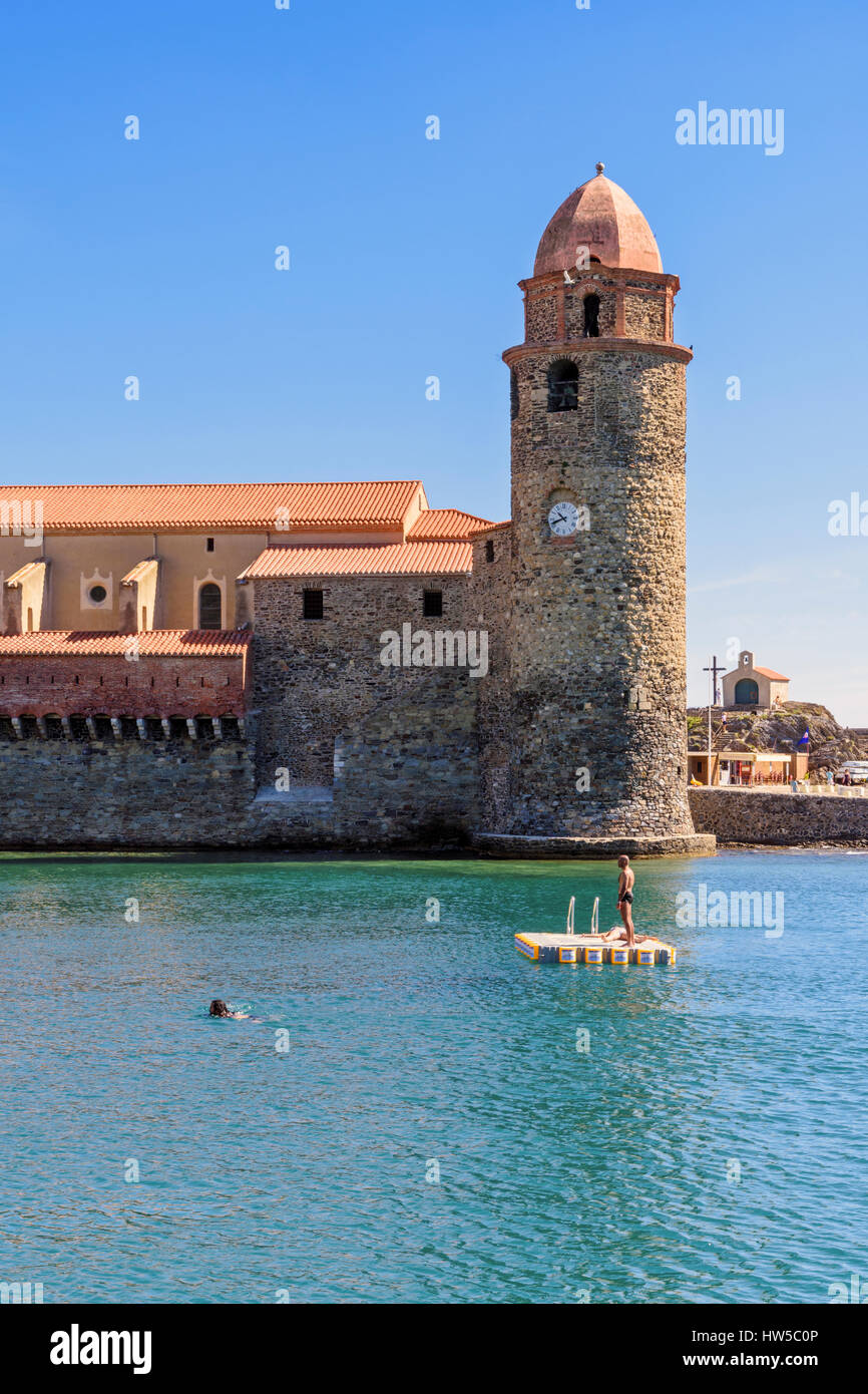 People on a pontoon overlooked by the bell tower of the Church of Notre Dame des Anges, Collioure, Côte Vermeille, France Stock Photo