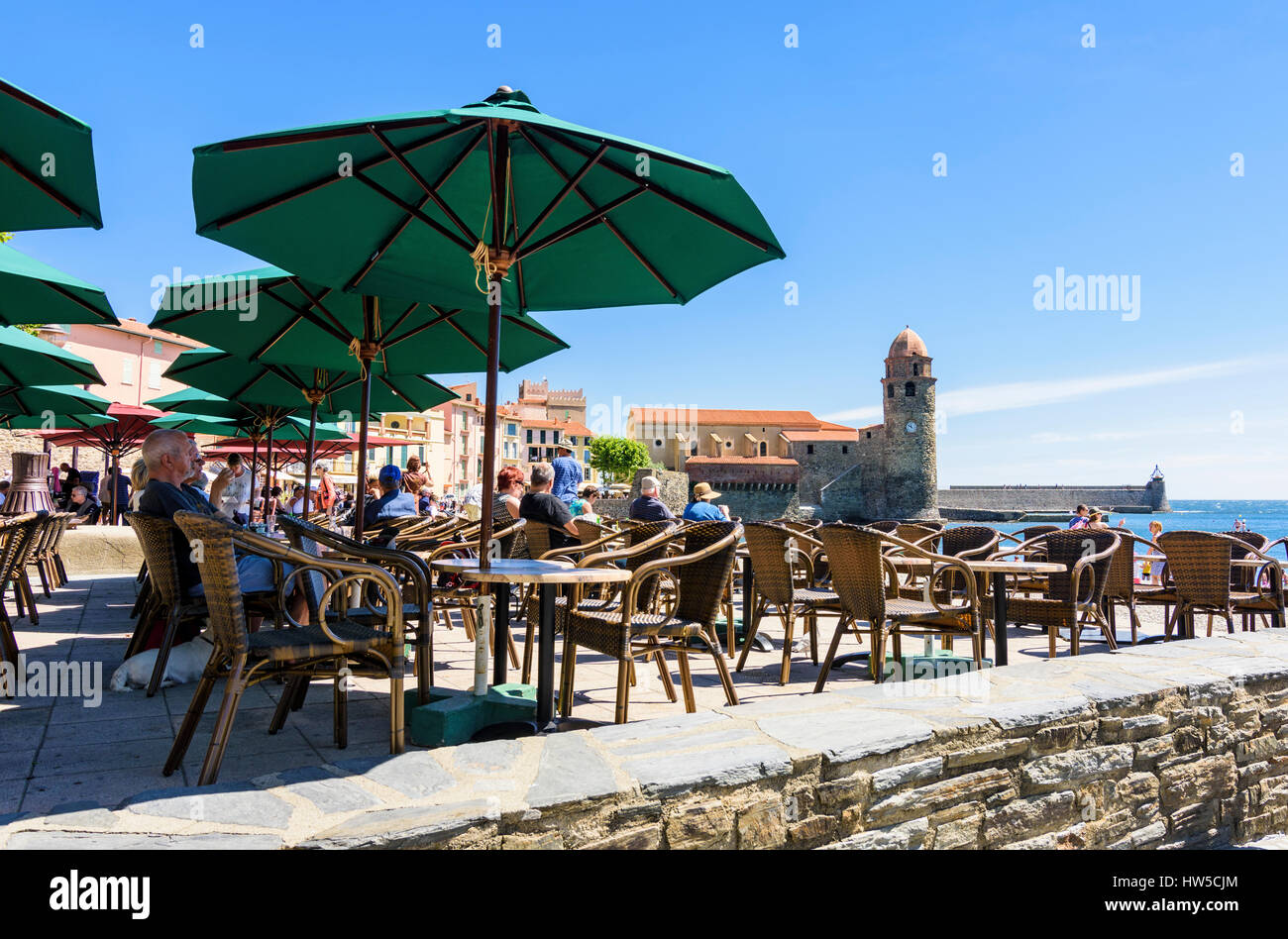 People at a seaside cafe overlooked by the bell tower of the Church of Notre Dame des Anges, Collioure, Côte Vermeille, France Stock Photo