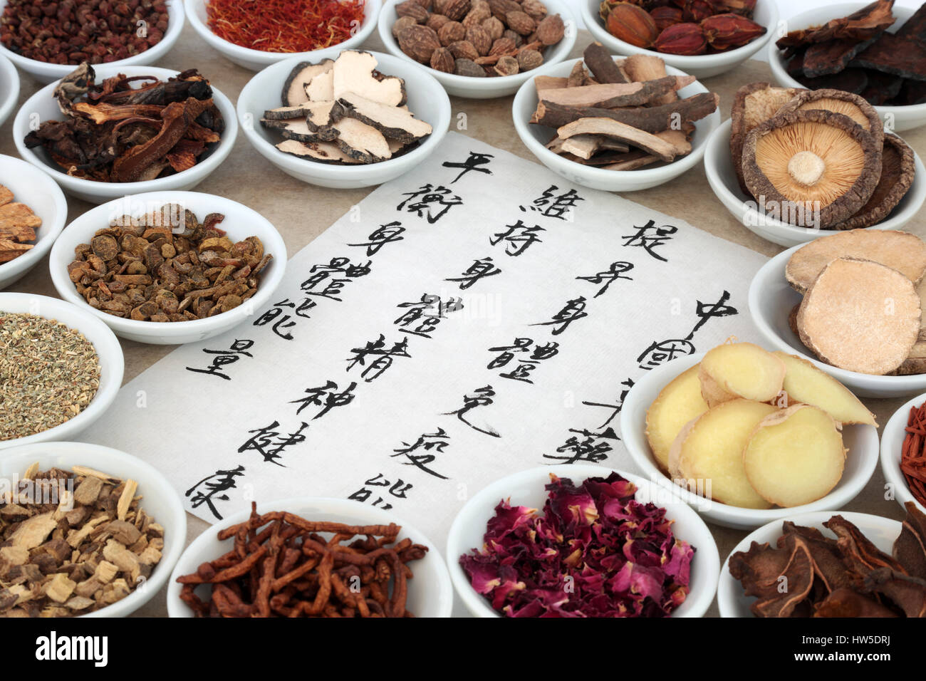 Traditional chinese medicinal herb selection in porcelain bowls with calligraphy script on rice paper. Translation describes chinese herbal medicine a Stock Photo