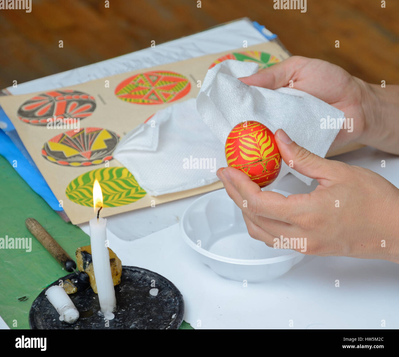 The human hands are wiping the ready painted egg near the candle burning. The Easter egg is decorated with a pattern using a wax-resist method. Stock Photo