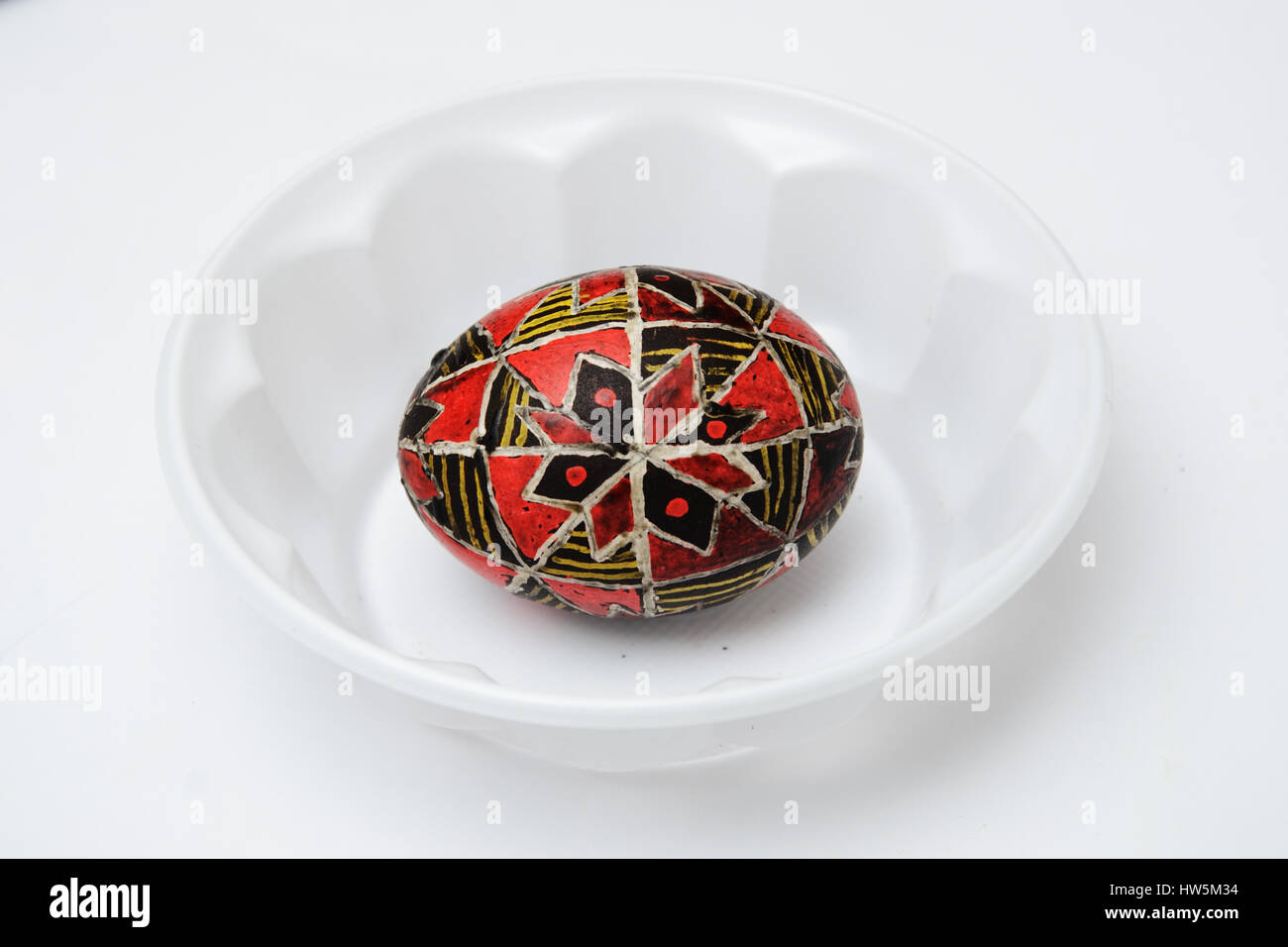 An Easter egg is decorated with traditional Ukrainian folk ornament using a wax-resist method. The pysanka is covered with wax and dyed red and yellow Stock Photo