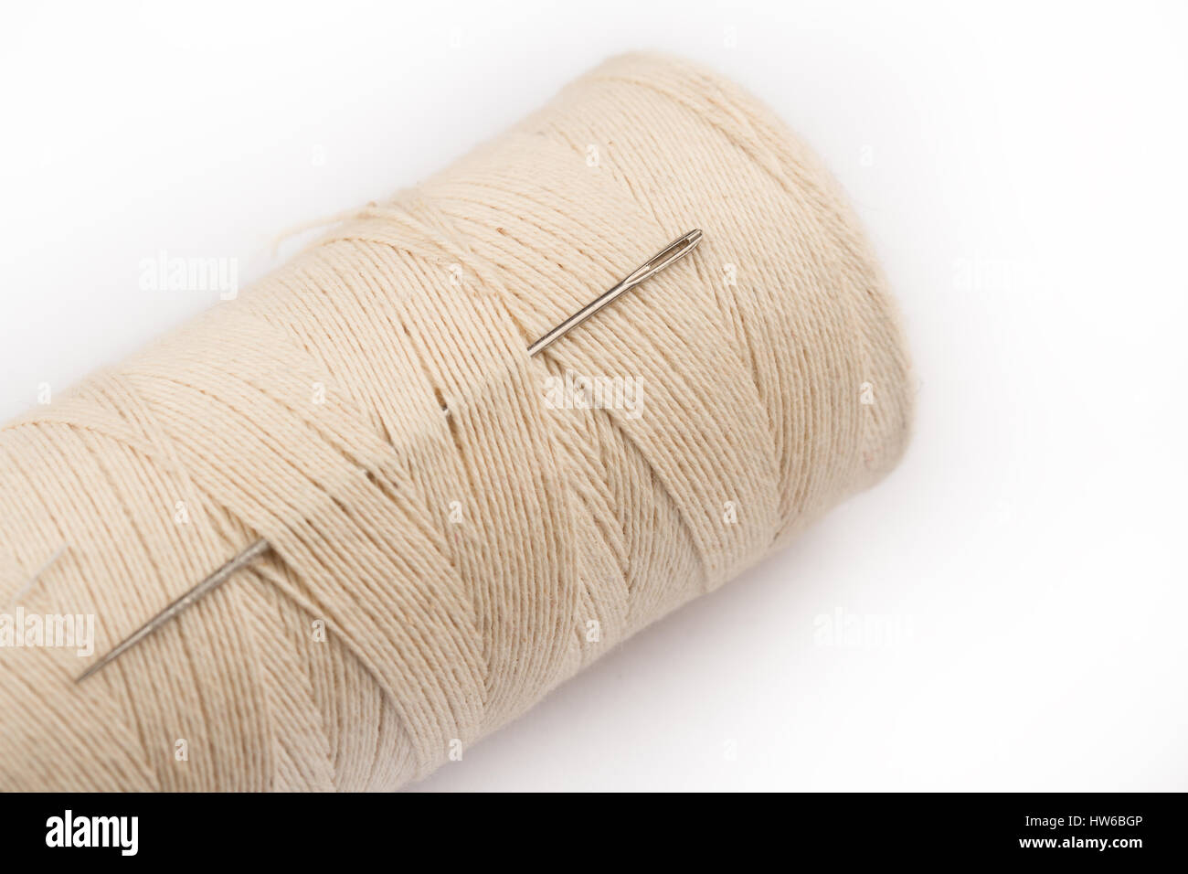 close up of metal sewing needle eye and spool on light colored thread ...