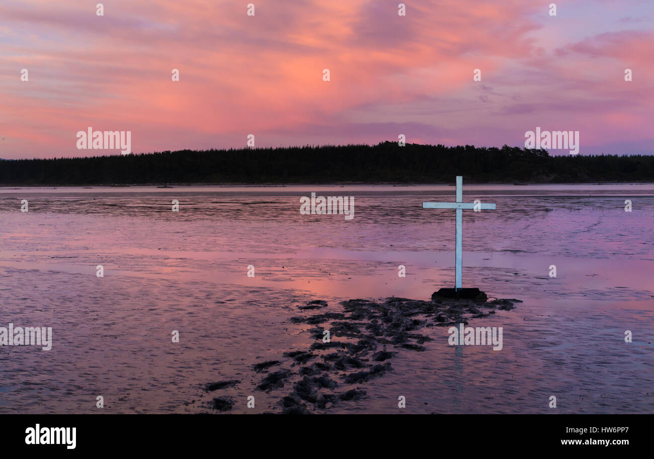 Some foot tracks in mud to a white cross. Stock Photo