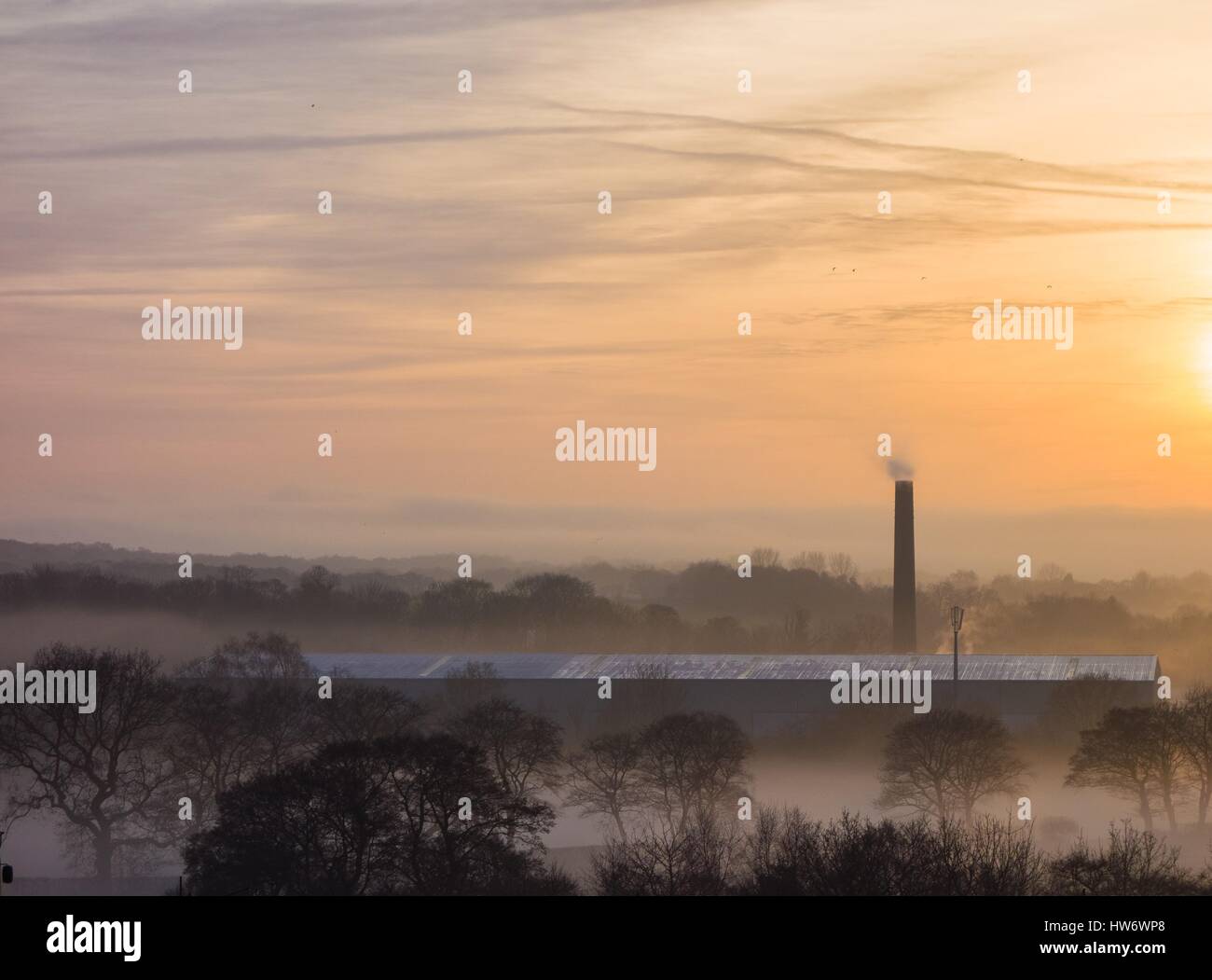 Factory chimney stack emerging from misty countryside at sunset Stock Photo