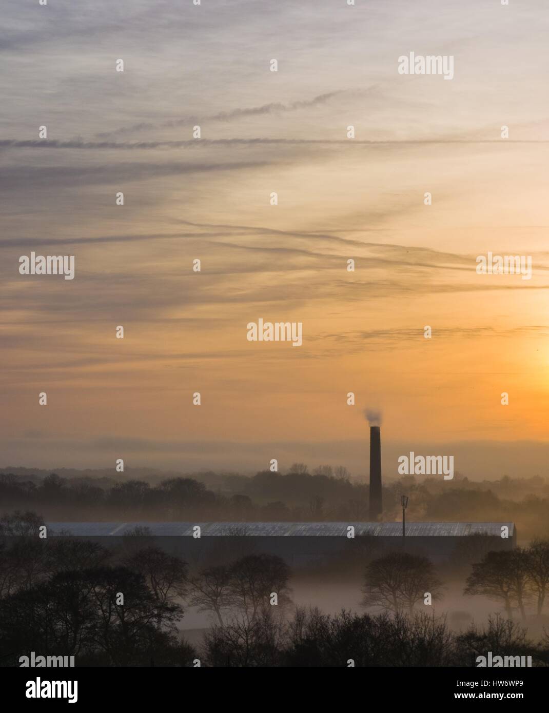 Factory chimney stack emerging from misty countryside at sunset Stock Photo