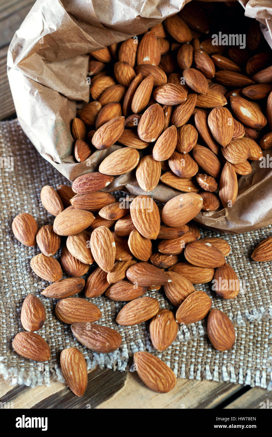 Almonds, pour out on wooden table out of a paper bag. Healthy eating. Stock Photo