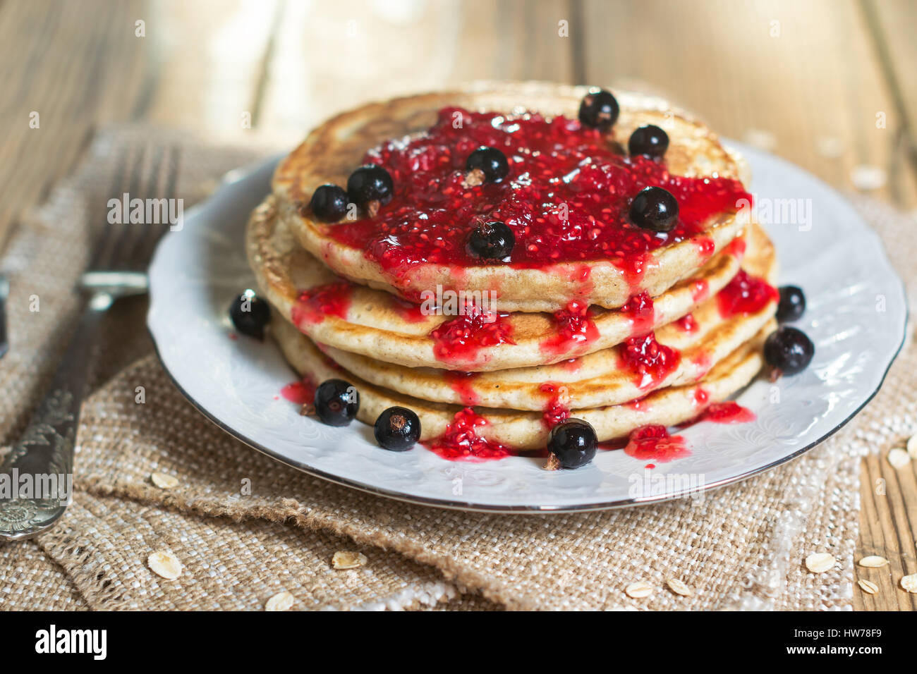 Delicious Oatmeal Pancake with raspberry jam and decorated with black currant. Natural sunlight in the background. Shallow DOF Stock Photo