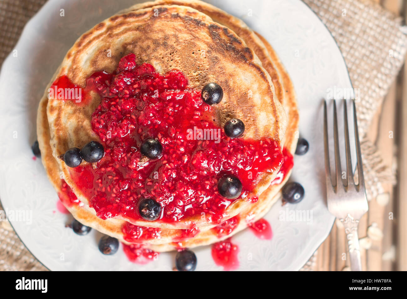 Delicious Oatmeal Pancake with raspberry jam and decorated with black currant. Top view, flat lay. Shallow DOF Stock Photo