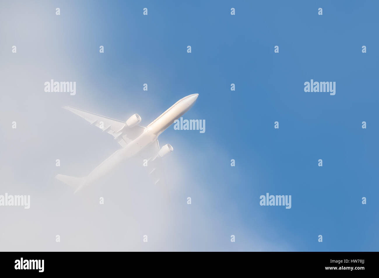 unmarked passenger jet punching through cloud into blue sky Stock Photo