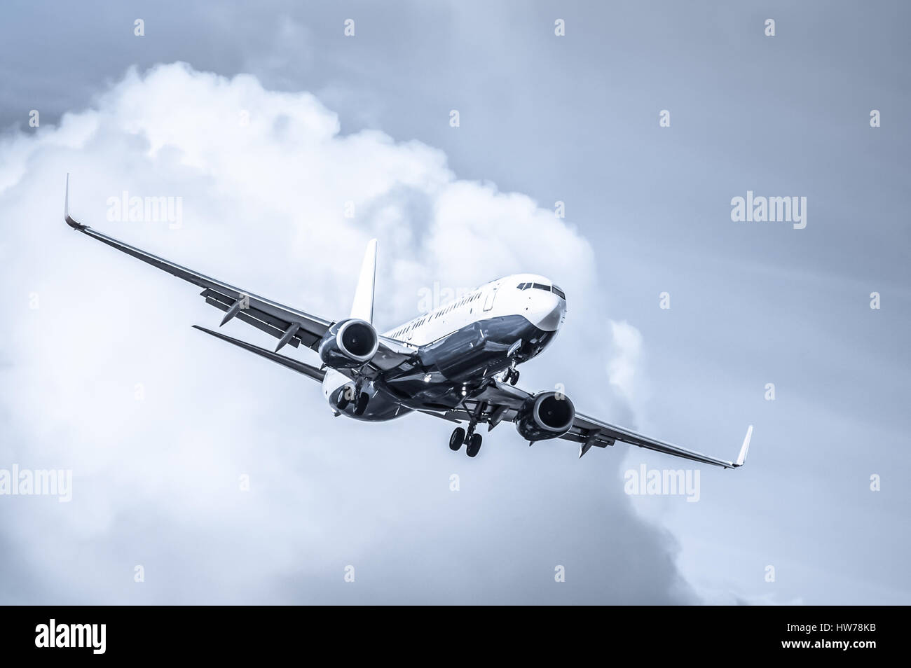 cool toned passenger jet on landing approach through a cloudy sky Stock Photo