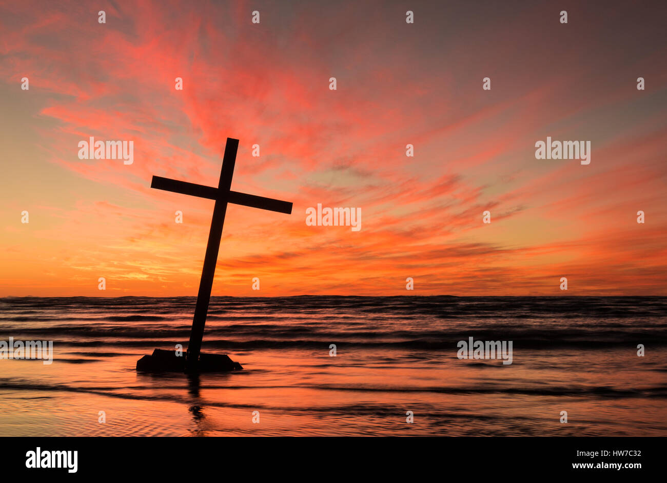 Black cross leaning over on a beach with a wonderful and colorful sky