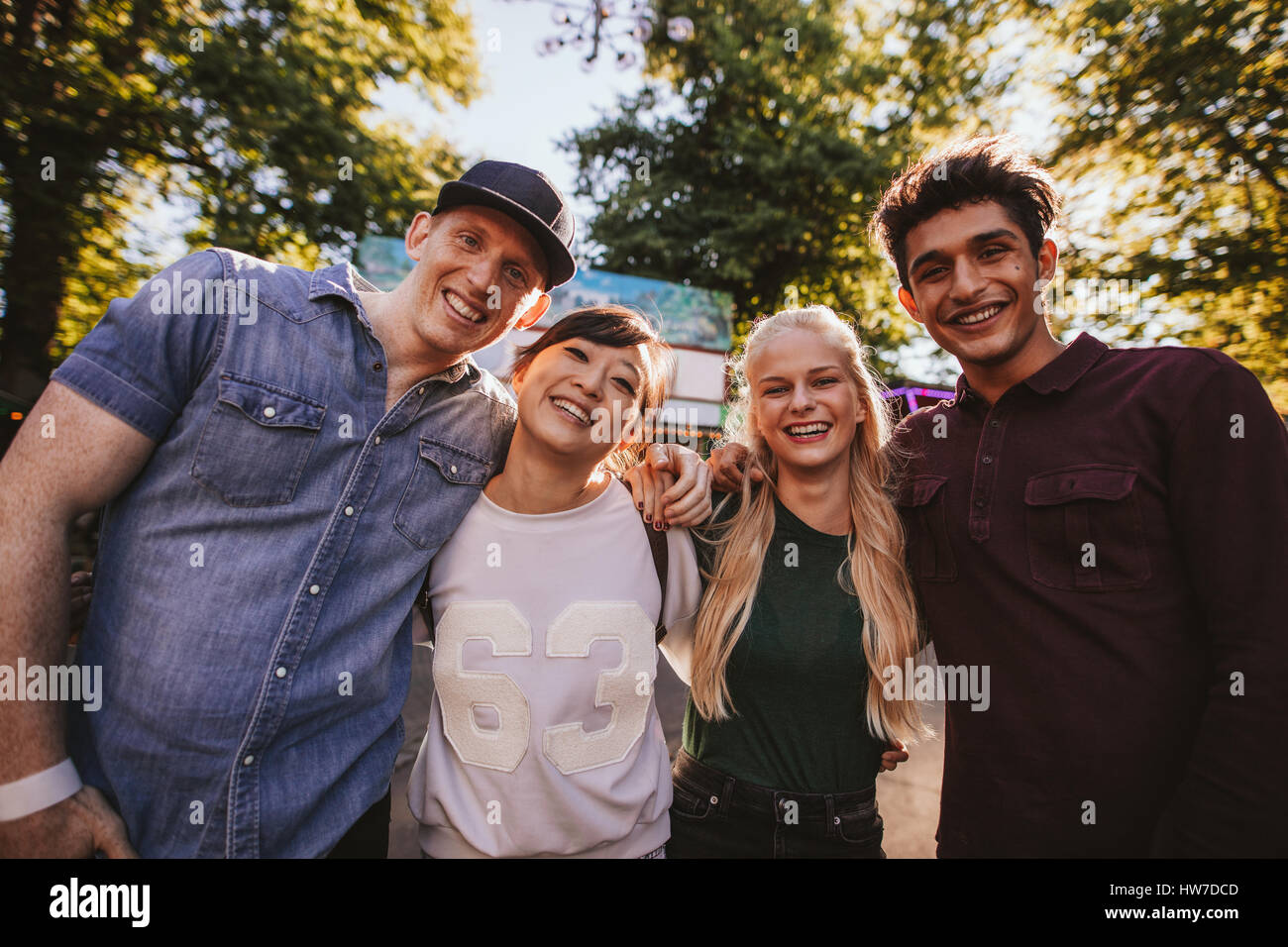 Multiracial friends standing together in amusement park. Group of friends in amusement park looking at camera and smiling. Stock Photo