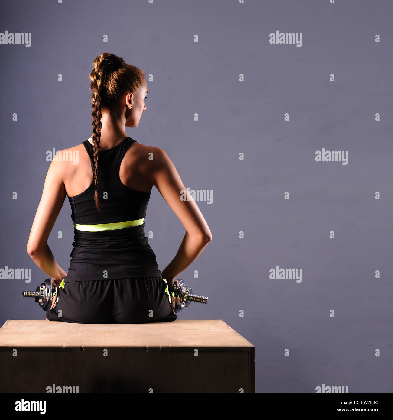 Fit young woman doing shoulder raises with dumbbells, isolated ongray background. Stock Photo