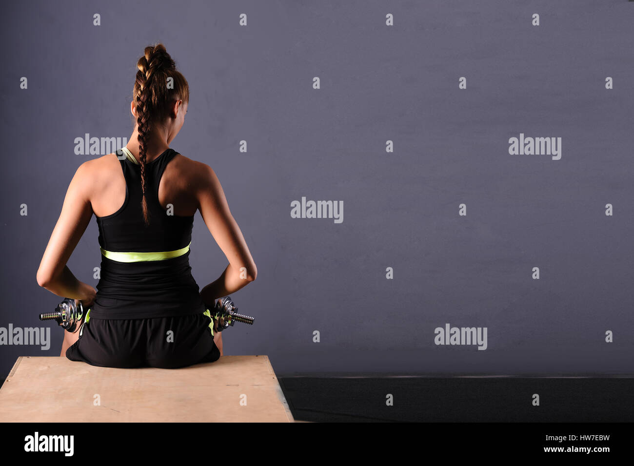 Fit young woman doing shoulder raises with dumbbells, isolated ongray background. Stock Photo