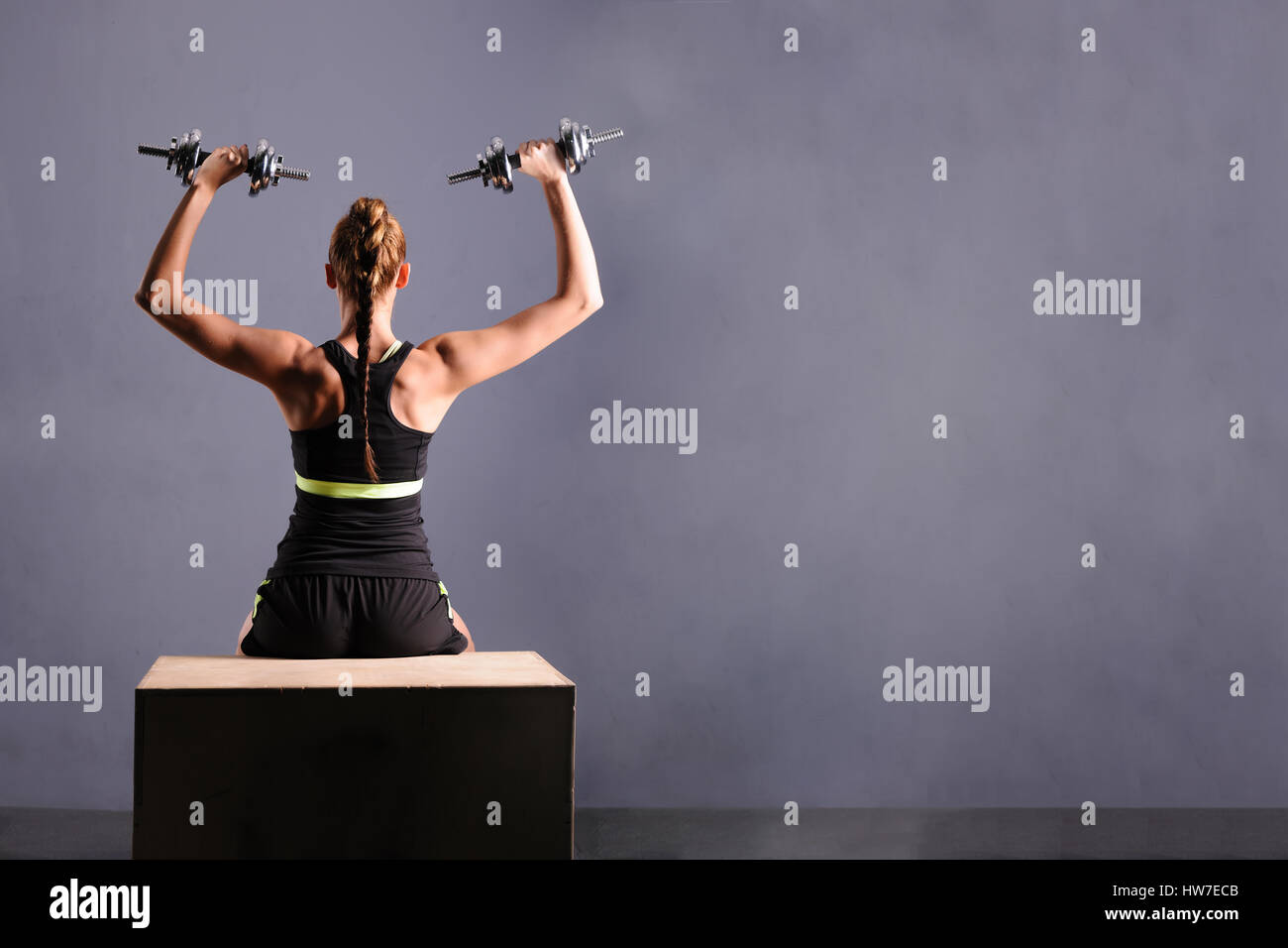 Fit young woman doing shoulder raises with dumbbells, isolated ongray background. Stock Photo