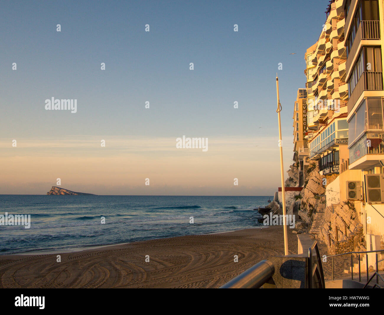 The hotel fronts in Benidorm Old Town are illuminated by an early morning sun. The iconic natural landmark of Benidorm Island sits in the background. Stock Photo