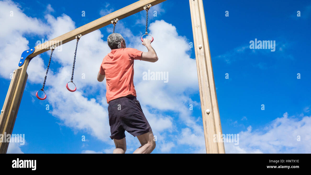 Mature man performing pull ups on rings in park Stock Photo