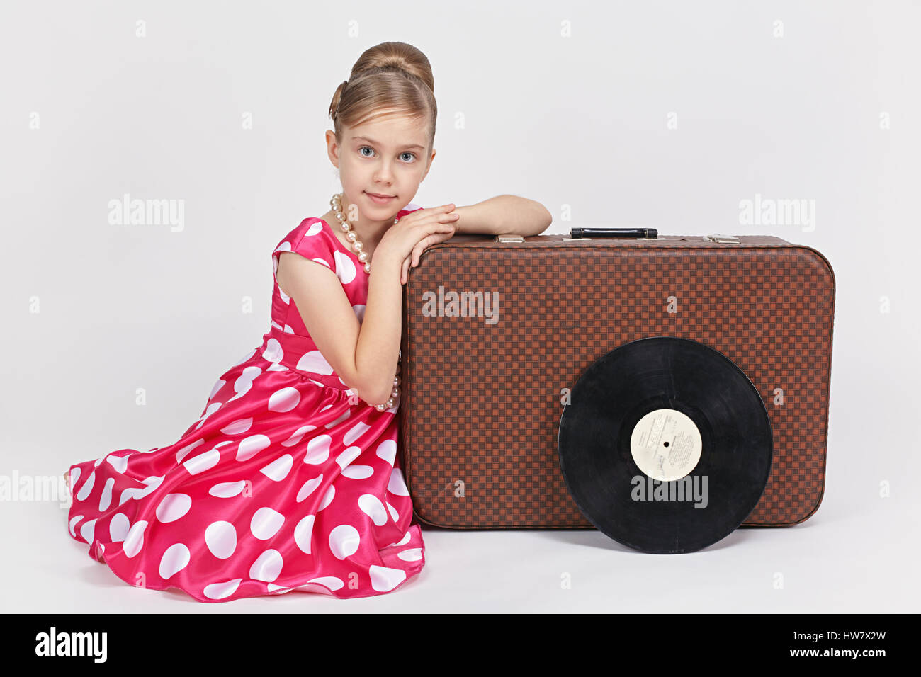 Dressed in a retro style girl sitting near an old suitcase Stock Photo